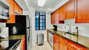 A compact kitchen with a window, stainless steel appliances, and wooden cabinets.