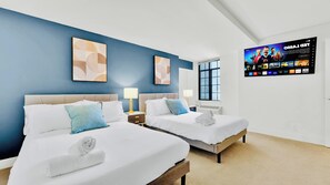 Ein Hotelzimmer mit zwei Betten, einem an der Wand befestigten Fernseher und Kunstwerken an den blauen Wänden.
