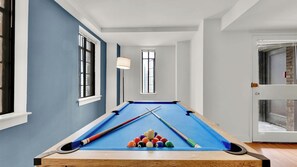 Ein Billardtisch in einem Raum mit blauen Wänden, einem Fenster und einer Tür.