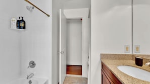 A bathroom with a white tiled shower, a bathtub, a vanity with a granite countertop, and a mirror.