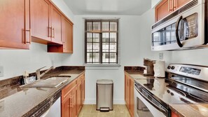 A compact kitchen with a sink, stove, microwave, and window with blinds.