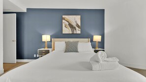 A hotel room with a large bed, two bedside tables with lamps, a headboard, and a wall-mounted painting.
