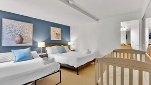 A hotel room with two beds, a crib, and artwork on the walls.