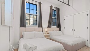 A hotel room with two beds, a wardrobe, and a window with curtains. - Modern 3-Bedroom Oasis in Center City (Philadelphia)