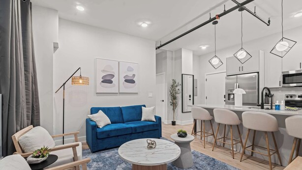 A modern living room with a blue sofa, a round coffee table, and a kitchen area with bar stools. - Modern 3-Bedroom Oasis in Center City (Philadelphia)
