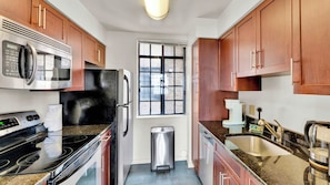 A compact kitchen with stainless steel appliances, a window with a view, and wooden cabinets. - Luxury 2BD | Center City | 4 Beds | Near LOVE Park (Philadelphia)