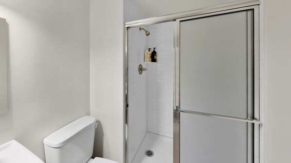 A bathroom with a toilet, a shower with a glass door, and toiletries on the wall.