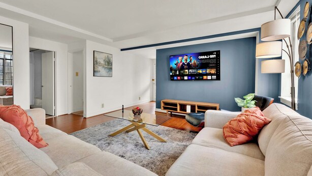 A modern living room with a flat-screen TV mounted on the wall, a sofa, a coffee table, and a wooden bench.