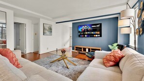 A modern living room with a flat-screen TV mounted on the wall, a sofa, a coffee table, and a wooden bench.
