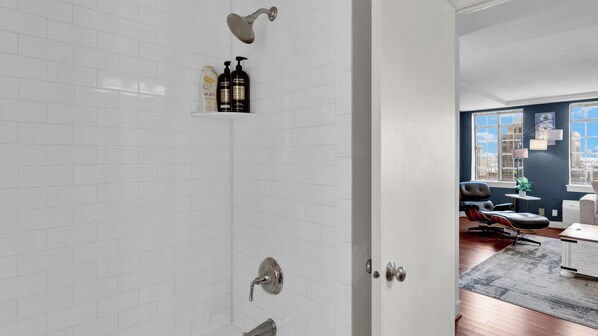 A modern bathroom with white subway tiles, a shower with a rain showerhead, and a vanity with toiletries.