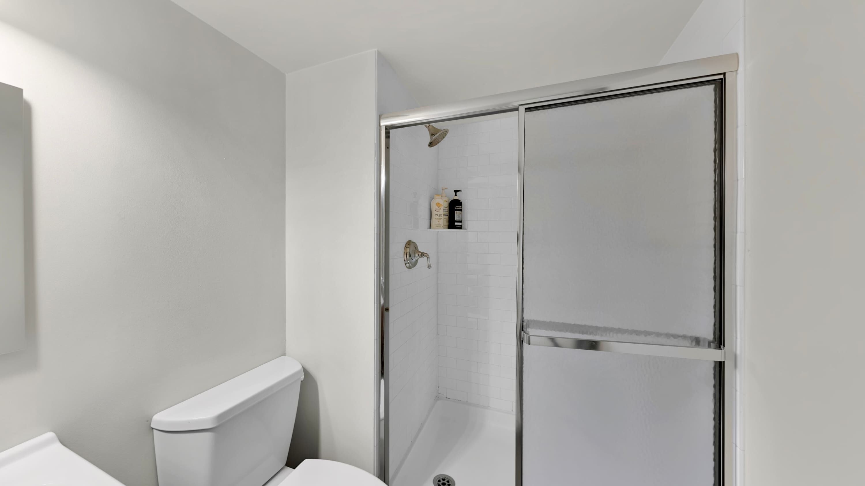 Une salle de bain comprenant des toilettes, une douche avec une porte en verre et une petite étagère avec des articles de toilette.