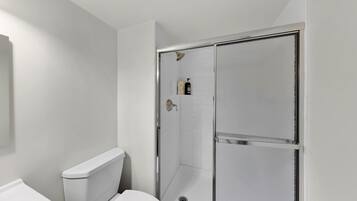 Une salle de bain comprenant des toilettes, une douche avec une porte en verre et une petite étagère avec des articles de toilette.