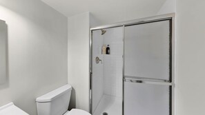 Ein Badezimmer mit Toilette, einer Duschkabine mit Glastür und einem kleinen Ablagebereich für Toilettenartikel.
