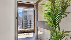 Ein Balkon mit Blick auf hohe Gebäude, einem Blumentopf und einer Tür, die in einen Innenraum führt.