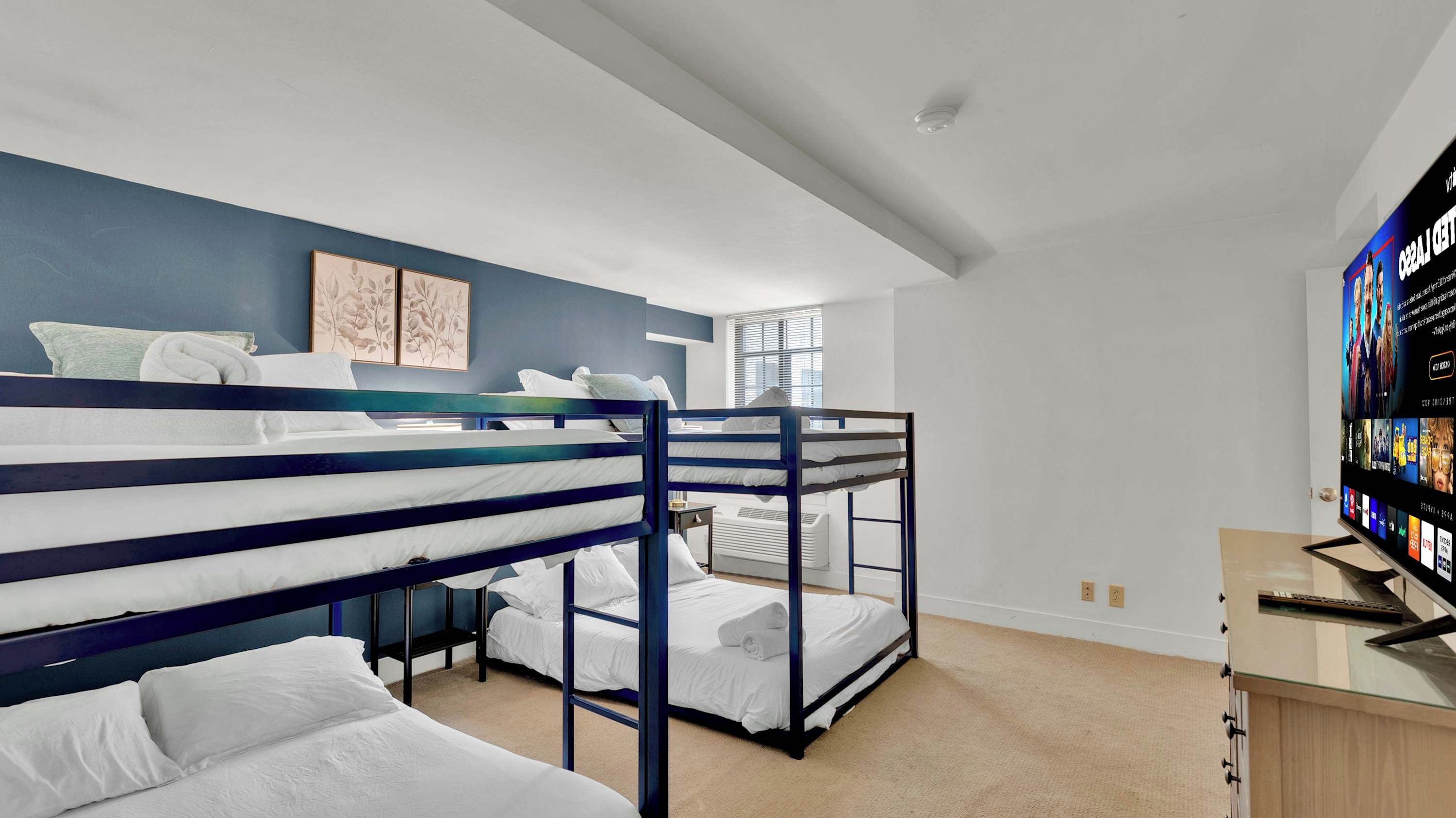 Une chambre avec des lits superposés, un téléviseur à écran plat et une fenêtre avec des stores.