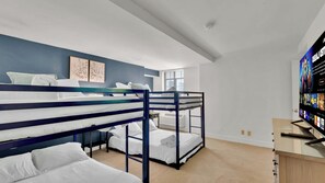 A room with bunk beds, a flat-screen TV, and a window with blinds.
