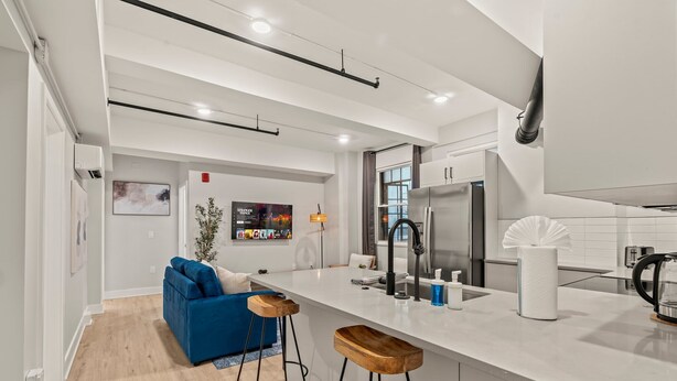 A modern kitchen with a white countertop, stainless steel appliances, and wooden stools.