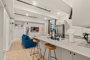 Una cocina moderna con encimera blanca, electrodomésticos de acero inoxidable y taburetes de madera.