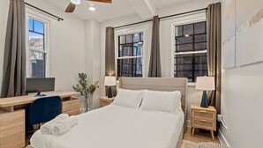A hotel room with a bed, desk, computer, and two bedside tables with lamps.