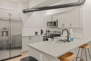 Una cocina moderna con electrodomésticos de acero inoxidable, armarios blancos y una isla central con taburetes.
