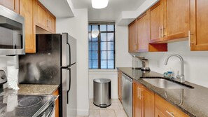 A compact kitchen with a microwave, refrigerator, stove, sink, and trash can.