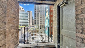 Blick von einem Balkon mit Metallgeländer auf einen Stadtblick mit hohen Gebäuden und einem Wandgemälde an einer Ziegelwand.