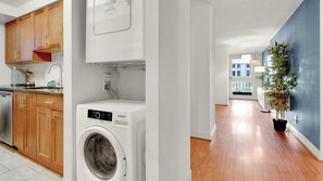 Eine moderne Küche mit Holzausstattung, einer integrierten Waschmaschine und Blick in den Wohnbereich.