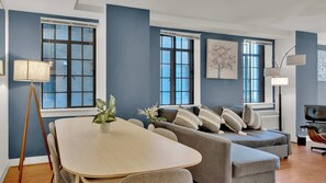 A modern living room with a round table, grey sofas, and a large window. - Stylish 2BD | Center City | 5 Beds | By JFK Plaza (Philadelphia)