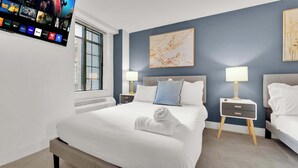 A hotel room with a large bed, two bedside tables, a TV mounted on the wall, and a window.