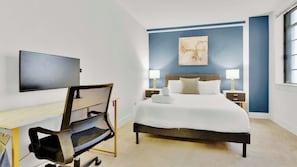 Ein modernes Schlafzimmer mit einem Bett, Nachttischlampen, einem Schreibtisch und einem Fernseher.