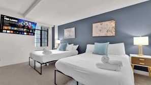 Une chambre d’hôtel avec deux lits, un téléviseur fixé au mur et des œuvres d’art accrochées aux murs.