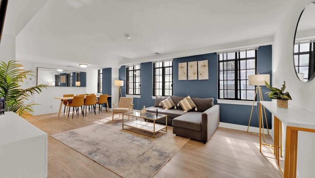 A spacious living area with a sofa, coffee table, and dining table, large windows, and a plant.