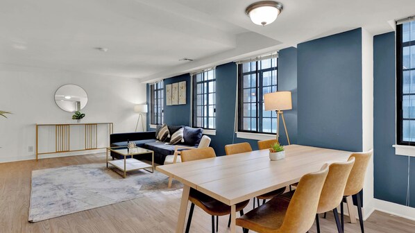 Una sala de estar moderna con un sofá, una mesa de comedor con sillas y un ventanal grande.