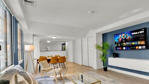 Ein modernes Wohnzimmer mit Fernseher, Essbereich und großem Fenster.