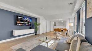 Uma sala de estar moderna com televisão de tela plana, uma área de jantar e uma cozinha ao fundo.