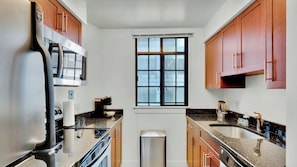 A modern kitchen with stainless steel appliances, wooden cabinets, and a window.