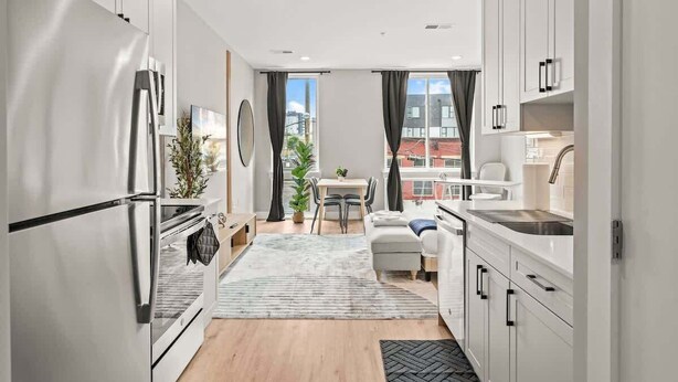 A modern kitchen with white cabinetry, a stainless steel refrigerator, and a dining area with a table and chairs. - Luxury Studio | 1 Bed | Northern Liberties (Philadelphia)