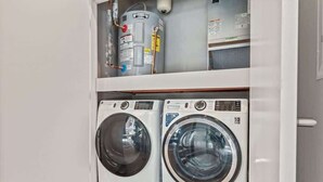 A laundry room with two front-loading washing machines and a water heater on the shelf above. - Luxury Studio | 1 Bed | Northern Liberties (Philadelphia)