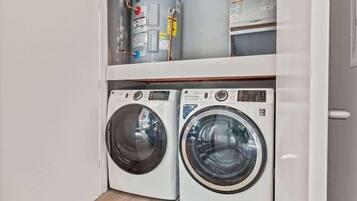 A laundry room with two front-loading washing machines and a water heater on the shelf above.