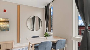 Ein moderner Essbereich mit einem Holztisch, grauen Stühlen, einem runden Spiegel und einem Blumentopf.