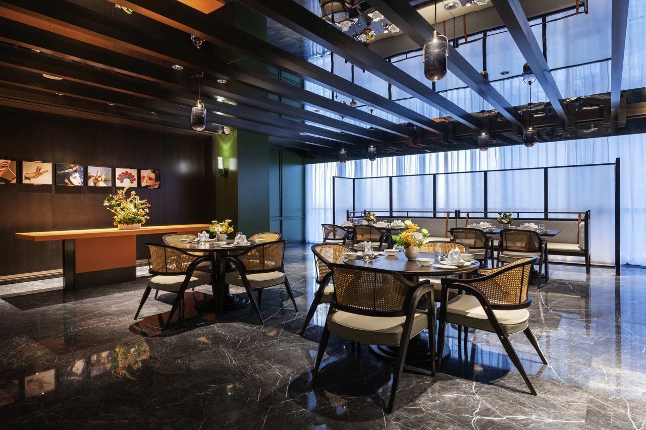 A modern dining area with high ceilings, exposed beams, and a mix of round and square tables with wicker chairs.