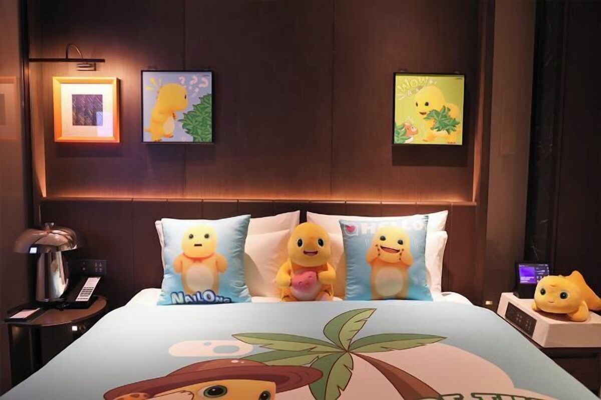 Ett hotellrum med en säng som har kuddar med motiv av tecknade figurer, ett sängbord med en lampa och inramade konstverk på väggen.
