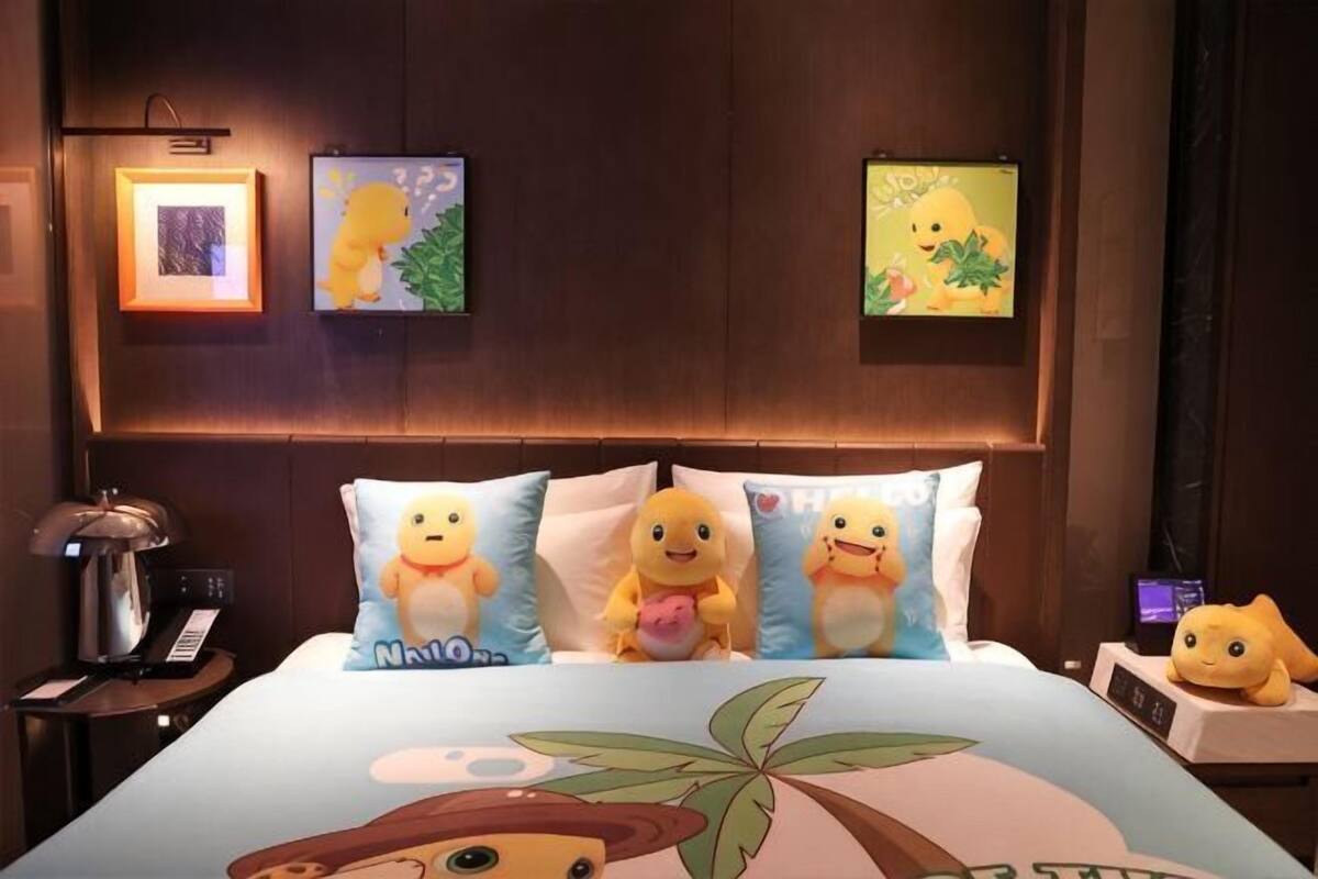 Ein Hotelzimmer mit einem Bett, das mit Kopfkissen mit Cartoon-Figuren ausgestattet ist, einem Nachttisch mit Lampe sowie gerahmten Bildern an der Wand.