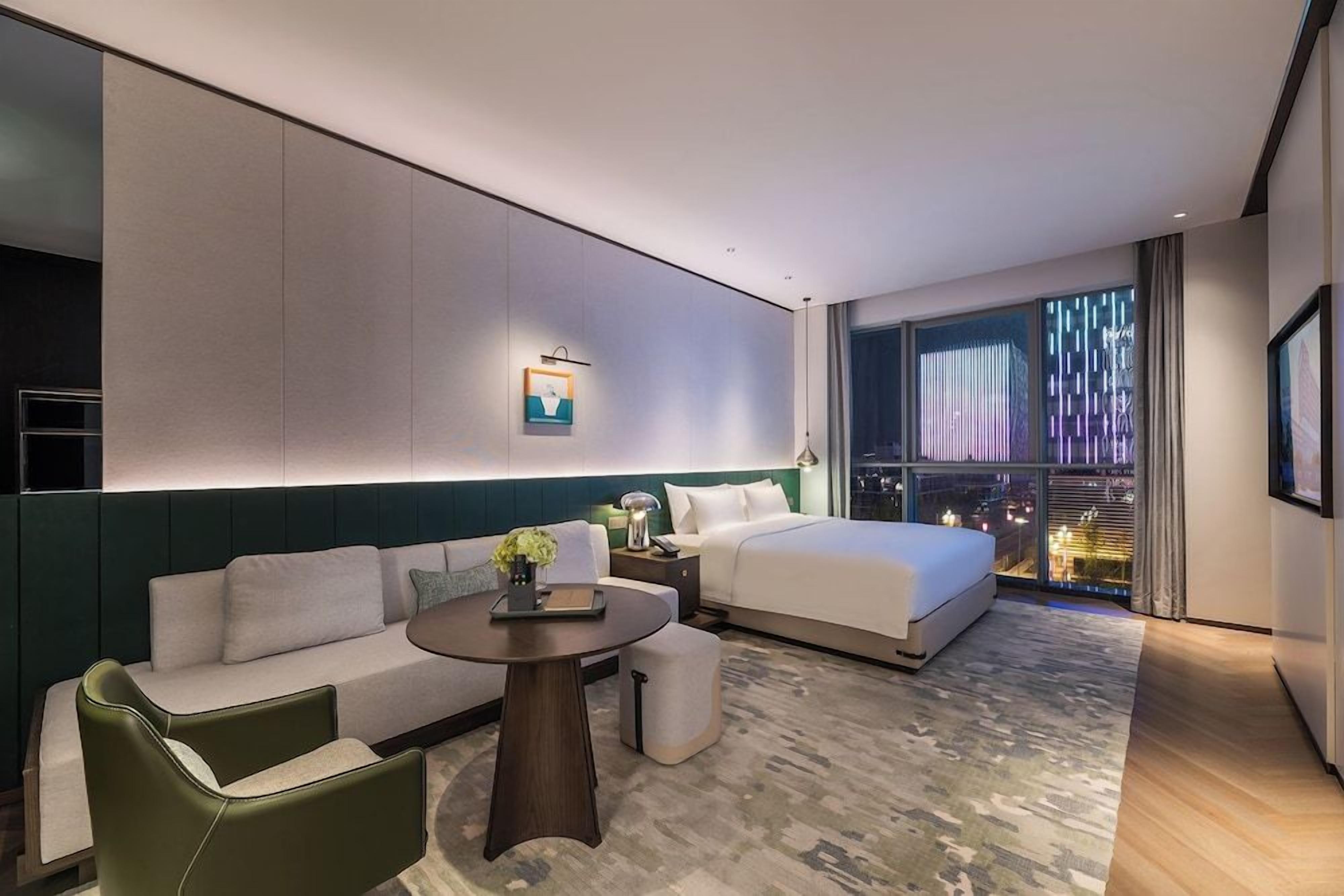 A modern hotel room with a bed, sofa, and a small table.
