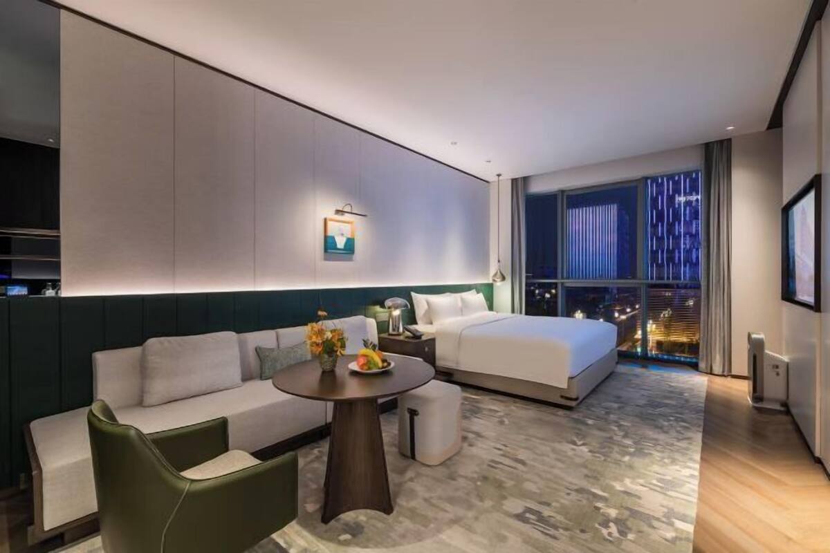 Ein modernes Hotelzimmer mit Bett, Sofa, Esstisch und Blick auf die Stadt.