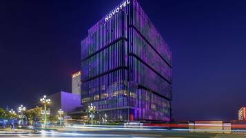 A modern hotel with a prominent 'NOVOTEL' sign, featuring a contemporary design with vertical lines and a glass facade.