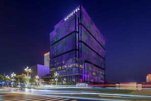 A modern hotel with a prominent 'NOVOTEL' sign, featuring a contemporary design with vertical lines and a glass facade. - Novotel Xian Xixian (Xianyang)