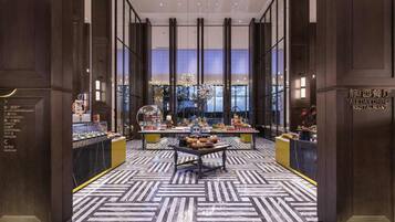 A modern hotel lobby with a central dining area, marble flooring, and a view of the cityscape through large windows.