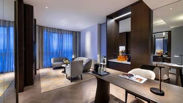 Une chambre d’hôtel moderne dotée d’un grand bureau, de sièges confortables, d’un coin cuisine et d’une grande fenêtre avec des rideaux.