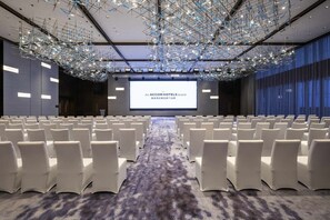 A conference room with rows of white chairs, a large screen displaying the ACCORHOTELS brand, and a modern chandelier. - Novotel Xian Xixian (Xianyang)